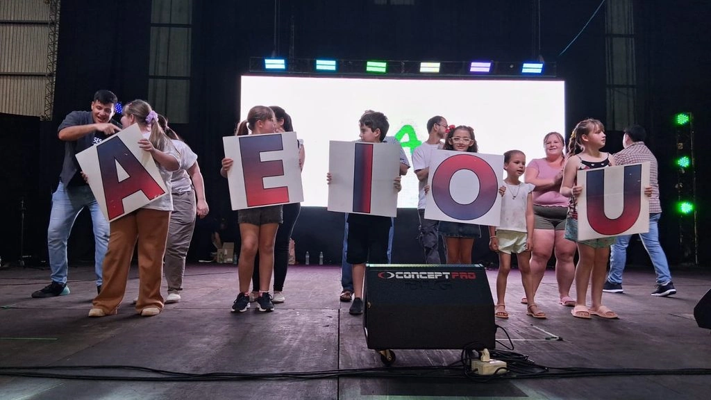 Niños y padres juegan con letras gigantes sobre el escenario.
