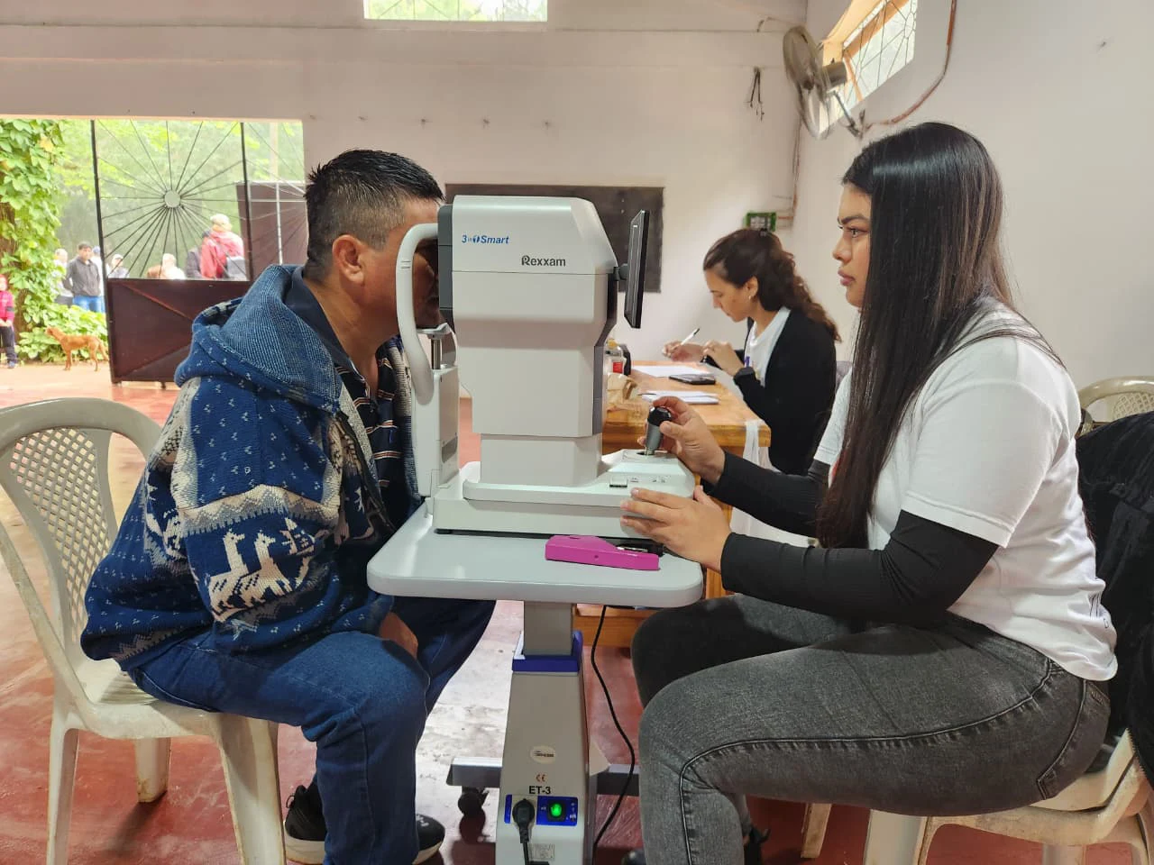 Oftalmóloga revisa los ojos de un joven vecino mediante un autorefractómetro. Mirar Mejor en Colona Polana.