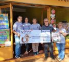 Equipo de la Agencia 316, frente al local, muestra sonriente el cheque del premio millonario de la Poceada Misionera.