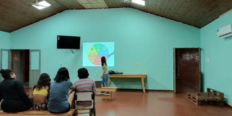 psicóloga del equipo de Juego Responsable explica un gráfico estadístico a jóvenes del hogar Papa Francisco.