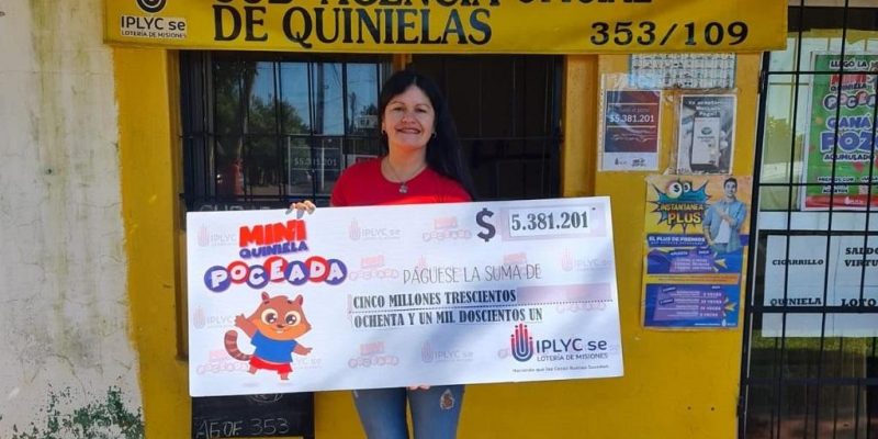 vendedora de la Mini Poceada millonaria frente a la sub agencia muestra sonriente el cheque